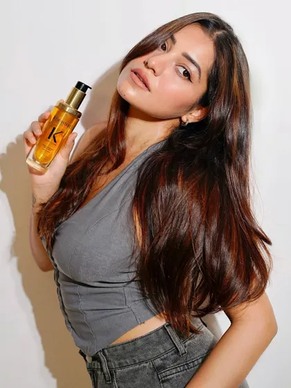 A client with beautiful, healthy hair holding a bottle of Kérastase hair oil. Our experts can recommend the perfect product for your hair type.