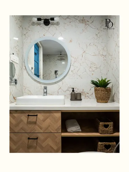 This bathroom vanity combines a herringbone-patterned wood drawer unit with open shelving for baskets, offering a mix of concealed and accessible storage. The round mirror softens the lines and adds a modern touch.