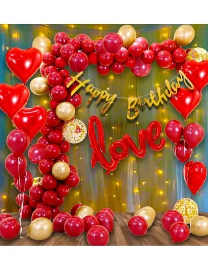 A classic romantic birthday decoration with a red and gold balloon arch, "Happy Birthday" and "Love" foil letters, and a backdrop of fairy lights.