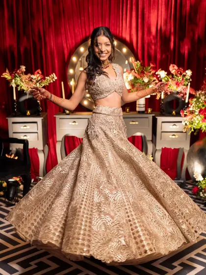 The bride twirls in her gorgeous golden lehenga at the 'Theatre of Love' Sangeet. The backdrop, designed to look like a vintage makeup room, adds to the retro, glamorous theme.