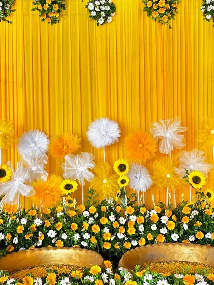 A cheerful Haldi backdrop combining a solid yellow drape with a mix of real sunflowers, white and yellow daisies, and delicate paper flowers.