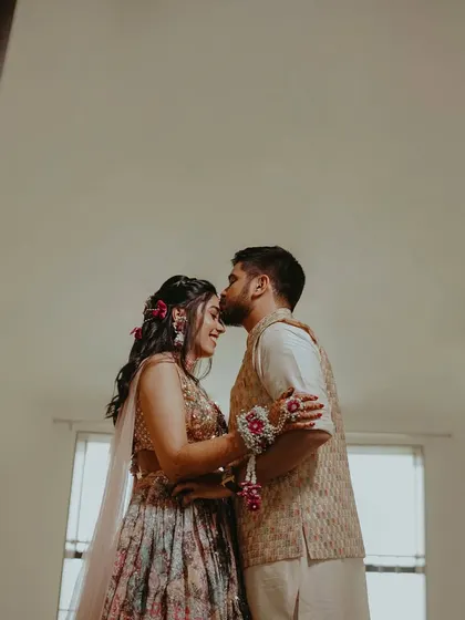 A tender forehead kiss, a quiet moment of love and affection shared between the couple during their Haldi ceremony, framed by a doorway.