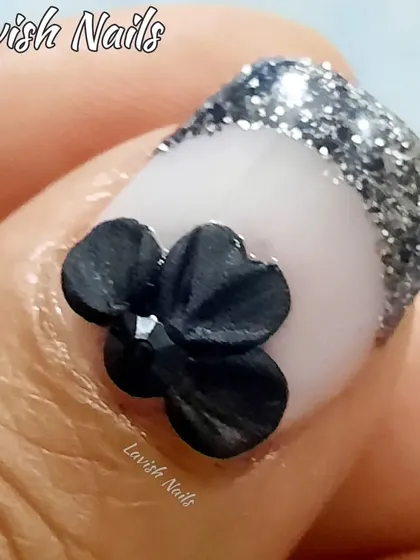 A close-up of a 3D black bow embellishment on a French tip with a silver glitter line, showcasing the fine details of custom nail art.