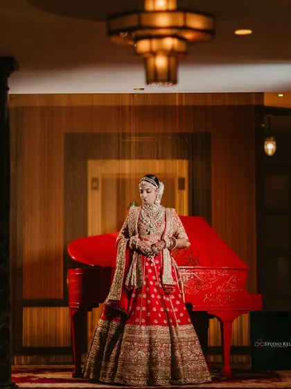 A stunning portrait of the bride in her red lehenga standing next to a vintage red piano at the Laxmi Niwas Palace.