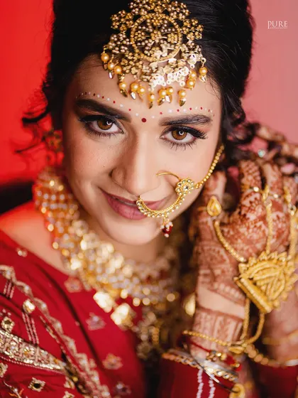 A close-up of the bride adjusting her nath. This candid-style portrait captures a natural gesture and showcases her beautiful henna and traditional jewelry.