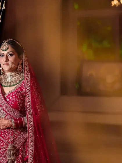 A full-length portrait of the bride in her stunning red lehenga, standing by a curtain of flowers, looking regal and elegant.