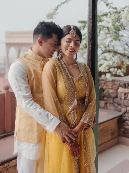 A happy, candid moment as the groom embraces the bride from behind on a balcony at Neemrana fort.