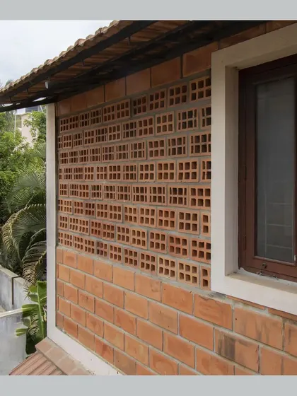 This exterior wall features a panel of hollow clay blocks set in a perforated pattern, creating a jaali screen. This allows for cross-ventilation while maintaining privacy, a key strategy for climate-responsive design.