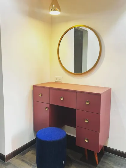 This standalone dressing table makes a statement with its bold magenta color and mid-century modern design, featuring tapered legs and brass knobs.