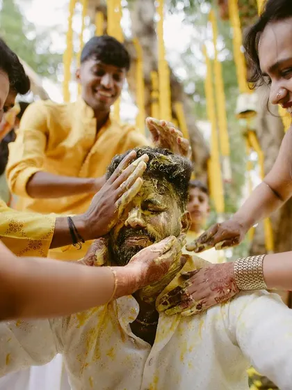 The groom being lovingly covered in turmeric paste by his family during the Haldi ceremony.