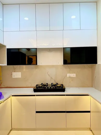A close-up of the cooking area in a white modular kitchen. The design includes a black hob, a marble-finish backsplash, and black-framed glass cabinets for a striking contrast.