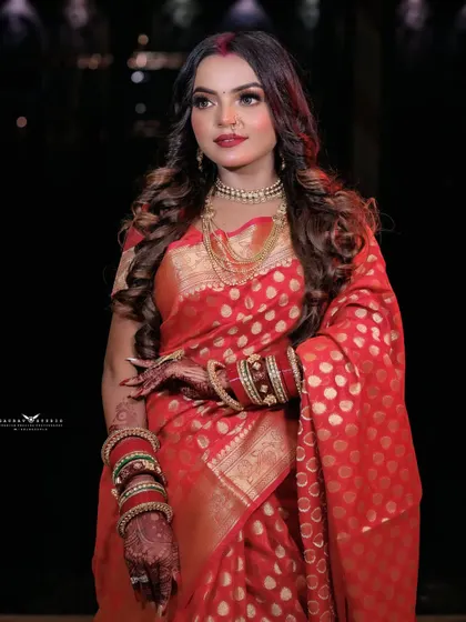 An elegant three-quarter portrait of the model in her red saree. The focus is on her poised stance and the beautiful gold jewellery that complements her outfit.