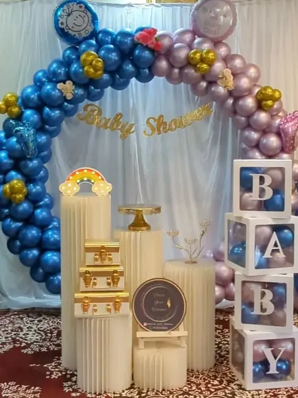 A baby shower decoration with a blue and purple balloon arch, 'BABY' blocks, and butterfly accents.