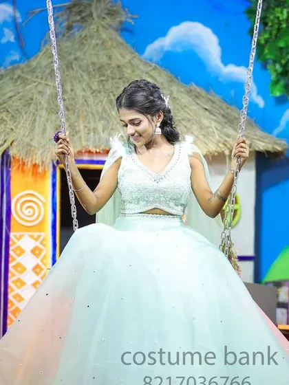 The young model in her light blue gown on a swing in the village-themed set.