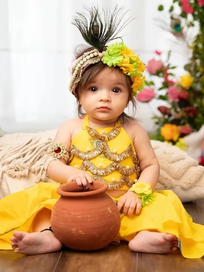 This little Radha is ready for the Janmashtami festivities, complete with a floral mukut and a mischievous pot.