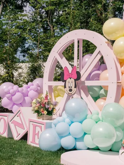 A close-up of the decor, showing a large pink wheel prop, "ONE" blocks, and a Minnie Mouse cutout nestled in pastel balloons.
