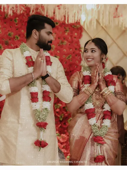 A happy couple exchanging greetings during their Hindu wedding ceremony, surrounded by a stunning wall of red flowers.