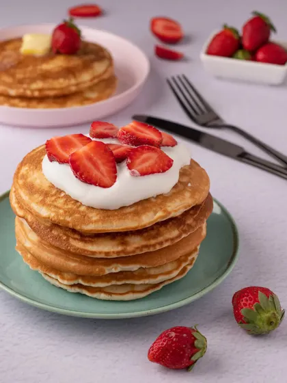 A classic breakfast or dessert: a stack of fluffy pancakes topped with fresh strawberries and cream. The clean, bright styling gives this shot a fresh and wholesome feel.