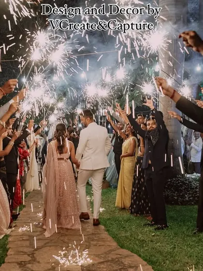 A beautiful shot of the couple walking through a path lit by sparklers held by their loved ones, creating a warm and celebratory welcome.