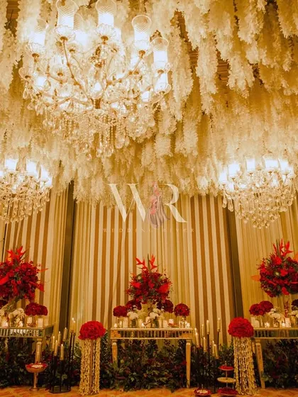 A stunning view of the floral installation, with a ceiling densely packed with hanging white flowers and chandeliers. The red arrangements below provide a powerful and romantic contrast.