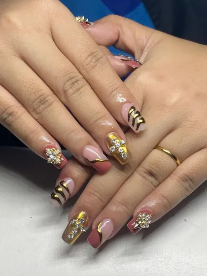 A bold and luxurious set. These square-shaped nails feature a mix of gold chrome, 3D textures, and large, cross-shaped rhinestone clusters.