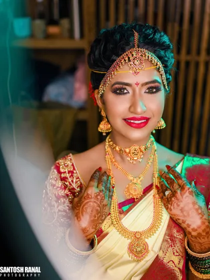 A radiant bridal portrait. The bride is fully ready in her traditional attire, with intricate gold jewelry and henna, smiling for the camera.
