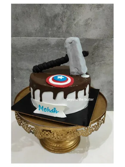 A cake for a fan of the God of Thunder. This design features Thor's hammer, Mjolnir, and Captain America's shield on a chocolate drip cake.