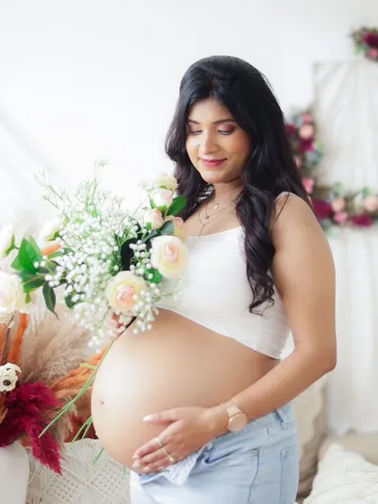 A sweet and casual portrait of a couple in a boho setting. The mom-to-be holds a bouquet of flowers, adding a touch of softness to the scene.
