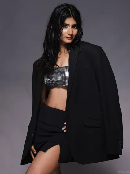 A model with the "wet look," wearing a silver top and black blazer, with a relaxed pose.