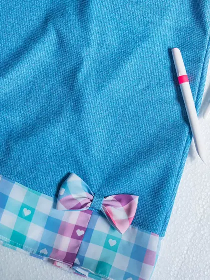 A close-up of the heart-printed checkered hem and bow on this unique denim dress.