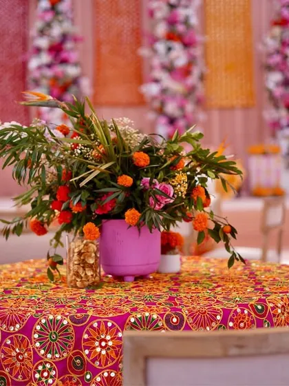 A guest table at the Phulkari Mehendi. The table is covered with a heavily embroidered and mirrored cloth, topped with a vibrant floral centerpiece in a pink vase, perfectly matching the theme.