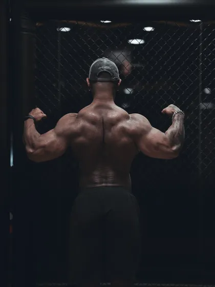 The rear double bicep pose against a cage, symbolizing the beast that is unleashed through training. This pose is critical for showing back thickness and hamstring detail.