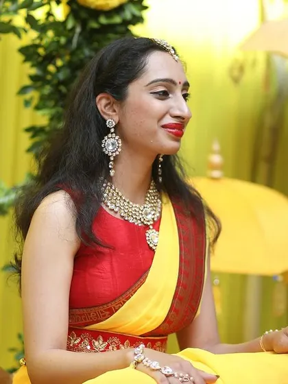 A moment of tradition during a Haldi ceremony, set against a backdrop of bright yellow drapes and marigold flowers.