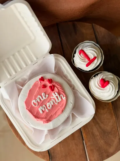 A close-up of the one-month anniversary combo, showing the textured pink frosting on the bento cake and the simple, sweet decorations on the cupcakes.