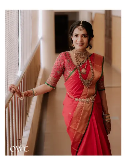 A full-length portrait of the bride in a corridor, her red saree vibrant and elegant.