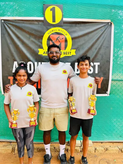 A coach with our two TS7 U-14 champions, Svar and Eshita, in front of our academy banner.
