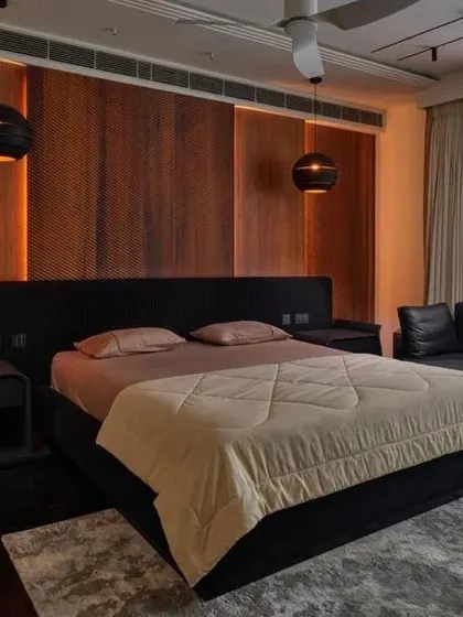 A bedroom that masterfully blends textures and tones. The warm wood paneling behind the bed, combined with soft backlighting, creates a cozy and inviting ambiance, perfect for a restful escape.