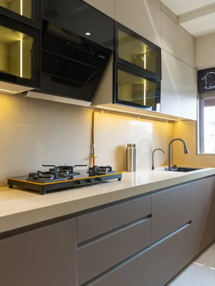 This cappuccino-toned kitchen in Vile Parle features handleless drawers for a clean, minimalist look. The black glass upper cabinets with internal lighting add a touch of drama and are perfect for displaying glassware.