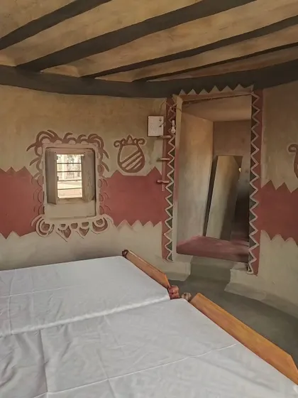 An interior view of a homestay bedroom, showing the clean lines of the bed against walls decorated with tribal patterns. The design balances rustic charm with comfort, creating a serene space for guests.