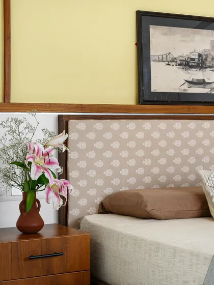 A close-up of the 'Poorna' guest bedroom, highlighting the fabric headboard and the warm, earthy tones of the bedside table and decor.