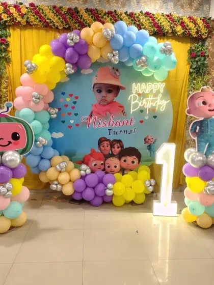 A Cocomelon themed birthday decoration for Nishant's first birthday. This setup features a colorful balloon arch, a custom backdrop, character cutouts, and a light-up number '1'.