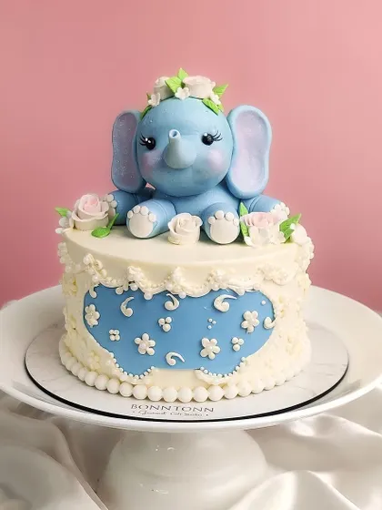 An absolutely adorable baby elephant cake. This light blue elephant with a floral crown sits atop a beautifully detailed buttercream cake.