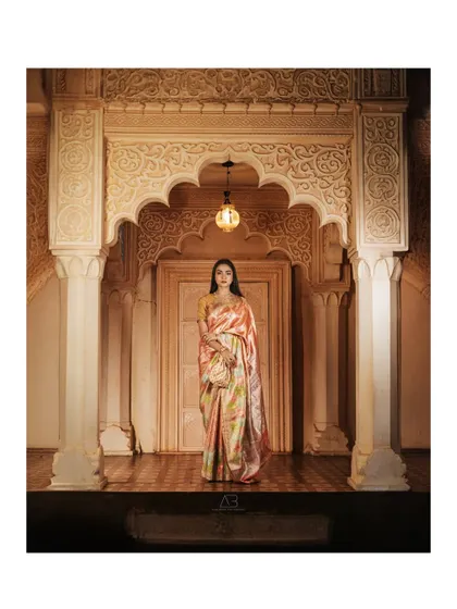 A wide shot that feels like a painting. The grand architecture and soft, warm lighting create a majestic frame for this classic, elegant saree portrait.