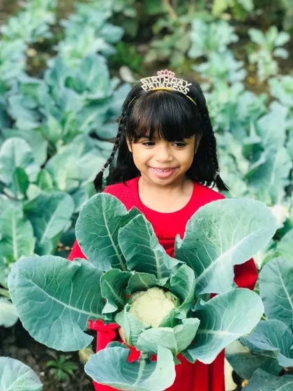A birthday princess holding a freshly picked cauliflower like a bouquet of flowers.