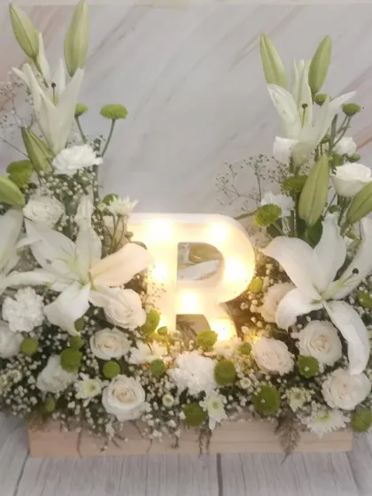 Make it personal for Mom with a light-up initial. This stunning arrangement of white lilies and roses is built around a glowing letter 'R', making it a truly special centerpiece.
