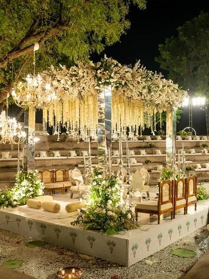 An enchanting nighttime ceremony setup in a stepwell-style venue, with a mandap illuminated by elegant chandeliers.