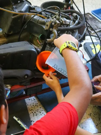 A student carefully pours oil into the engine using a funnel and measuring cup. This teaches them the basics of servicing and maintaining an engine.