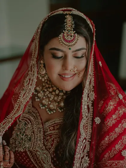 A serene bridal portrait. The bride's eyes are closed as she soaks in the moment, her intricate red lehenga and jewelry looking stunning.