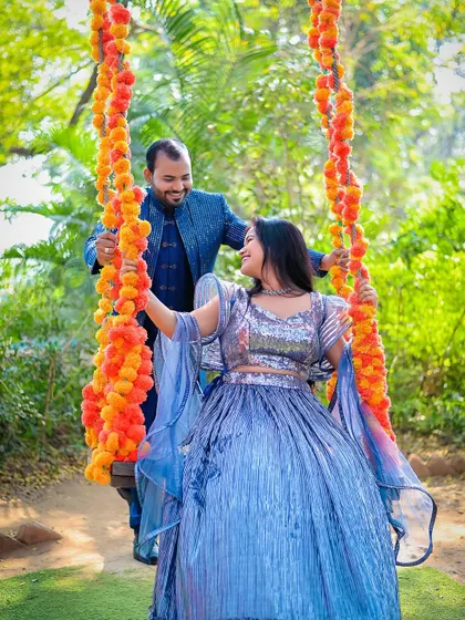 A joyful pre-wedding shot of a couple on a swing decorated with marigold flowers. The groom pushes the swing as they share a happy glance, perfectly capturing a moment of shared fun and affection.