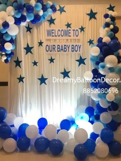 A beautiful backdrop I created to welcome a baby boy. It features a white curtain with blue stars, a "Welcome to our Baby Boy" sign, and is framed by an organic balloon garland in shades of blue and white.